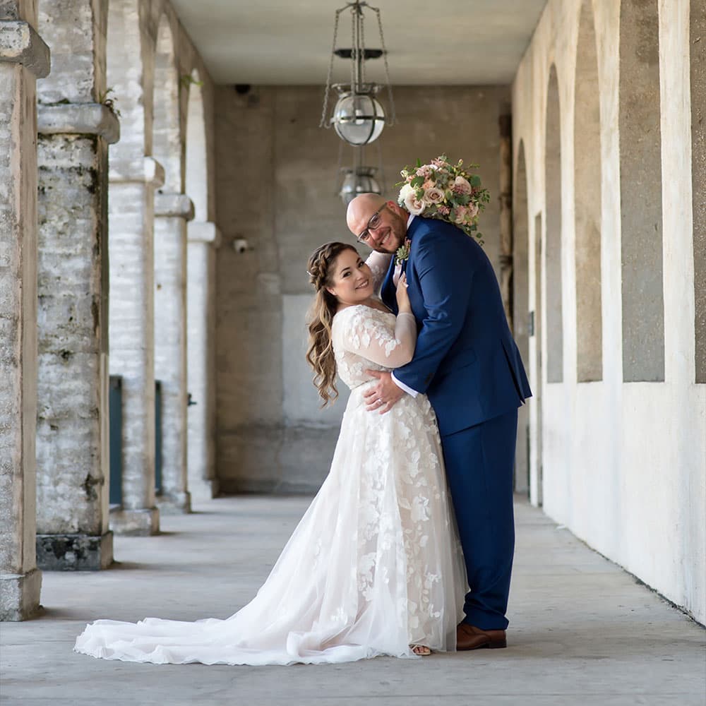 A bride and groom embrace in a charming archway, surrounded by soft lighting and elegant architecture.