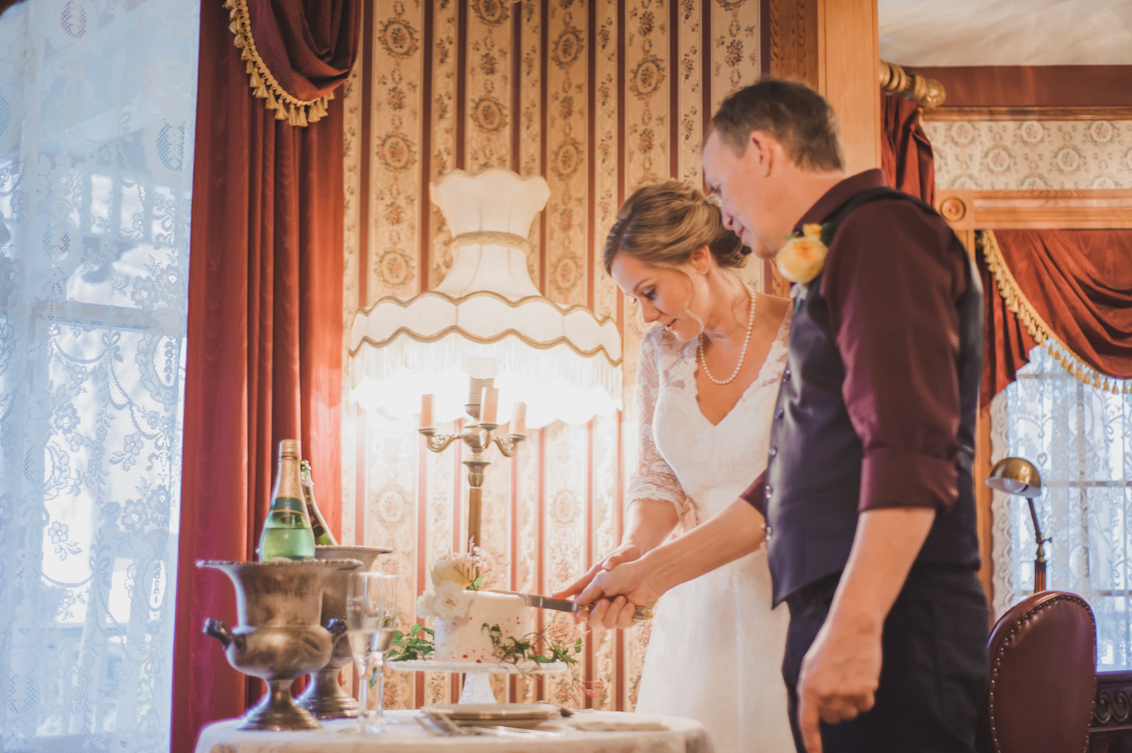 A bride and groom are cutting their wedding cake in a warmly decorated room.