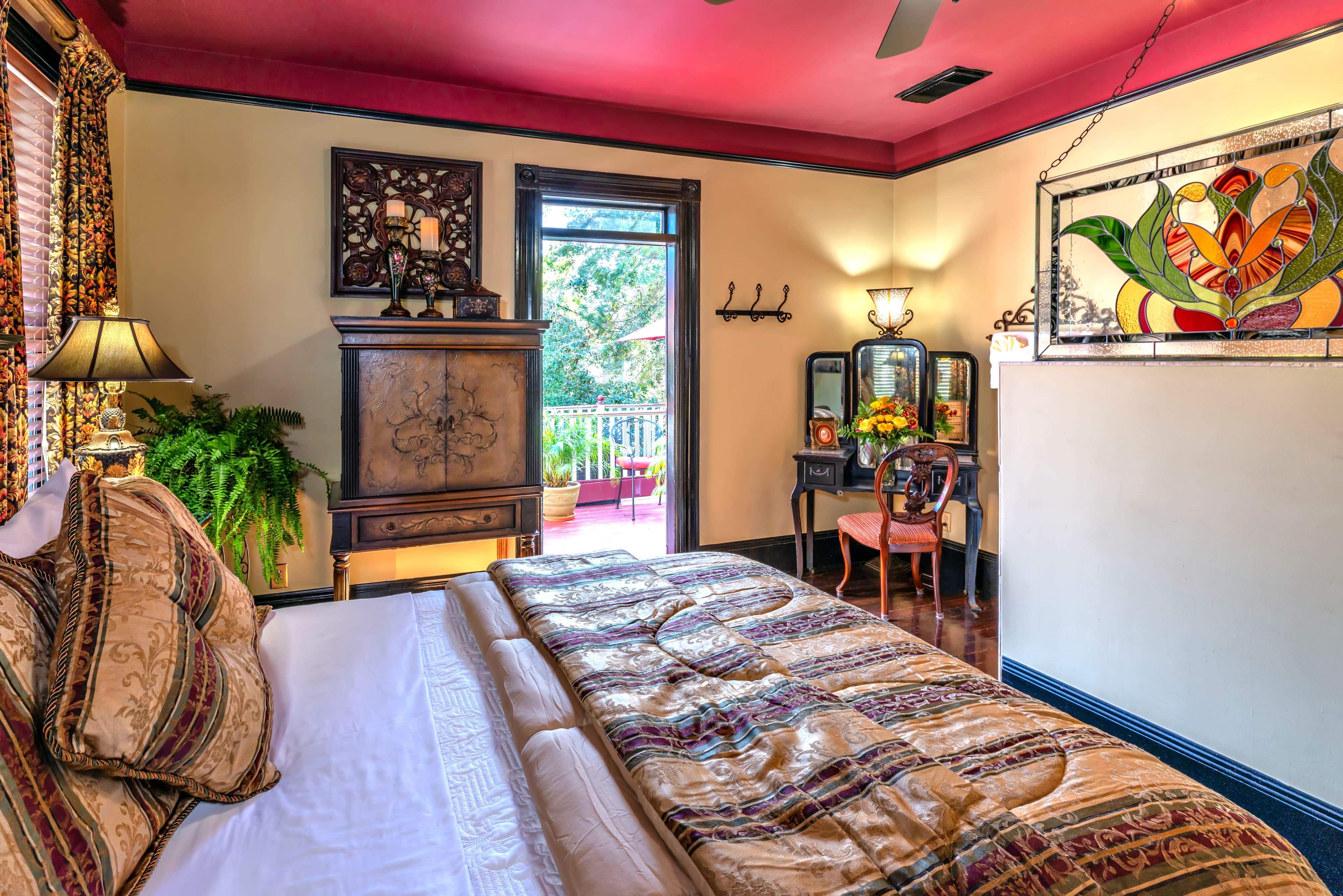 Cozy bedroom with a decorative stained glass window, antique furniture, and a vibrant pink ceiling.