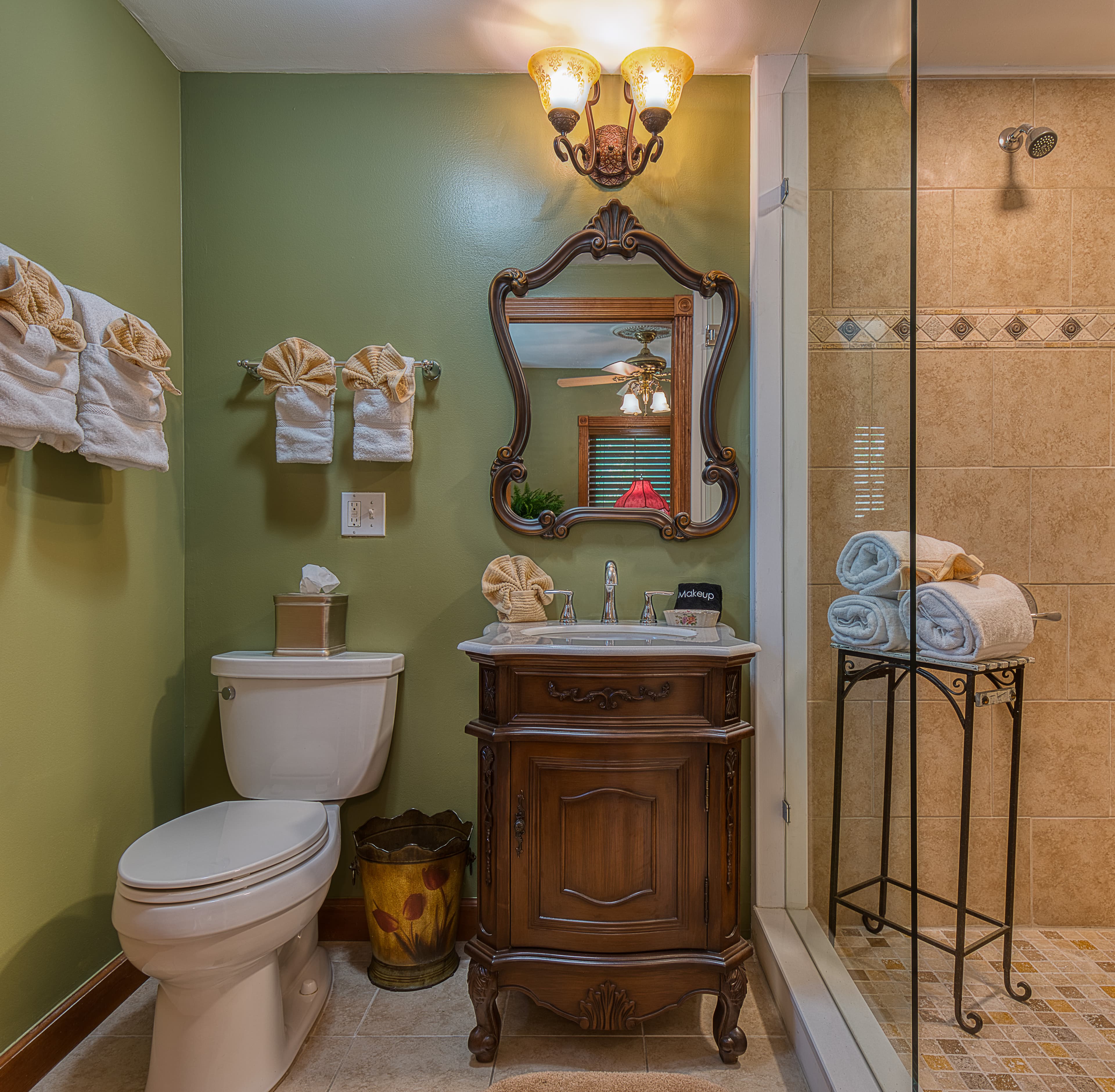 A stylish bathroom featuring green walls, a wooden vanity, and a glass shower.