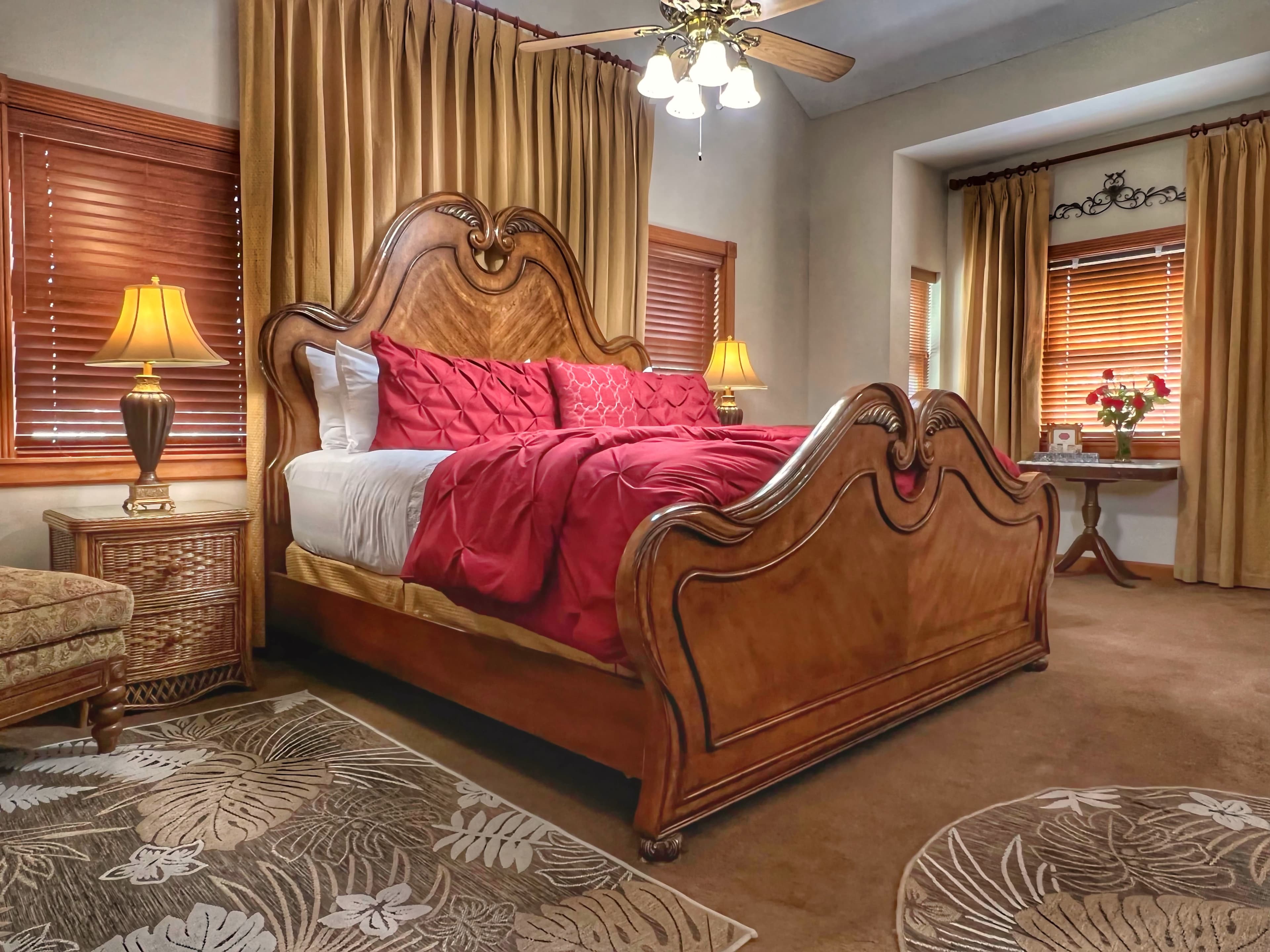 Cozy bedroom with a wooden bed, red bedding, a nightstand lamp, and elegant curtains.