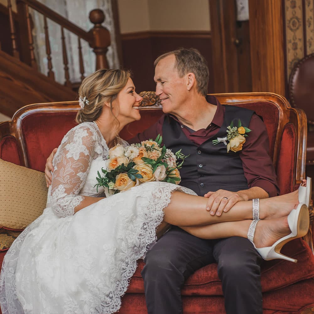 A joyful couple shares an intimate moment on a vintage couch, surrounded by floral decorations.