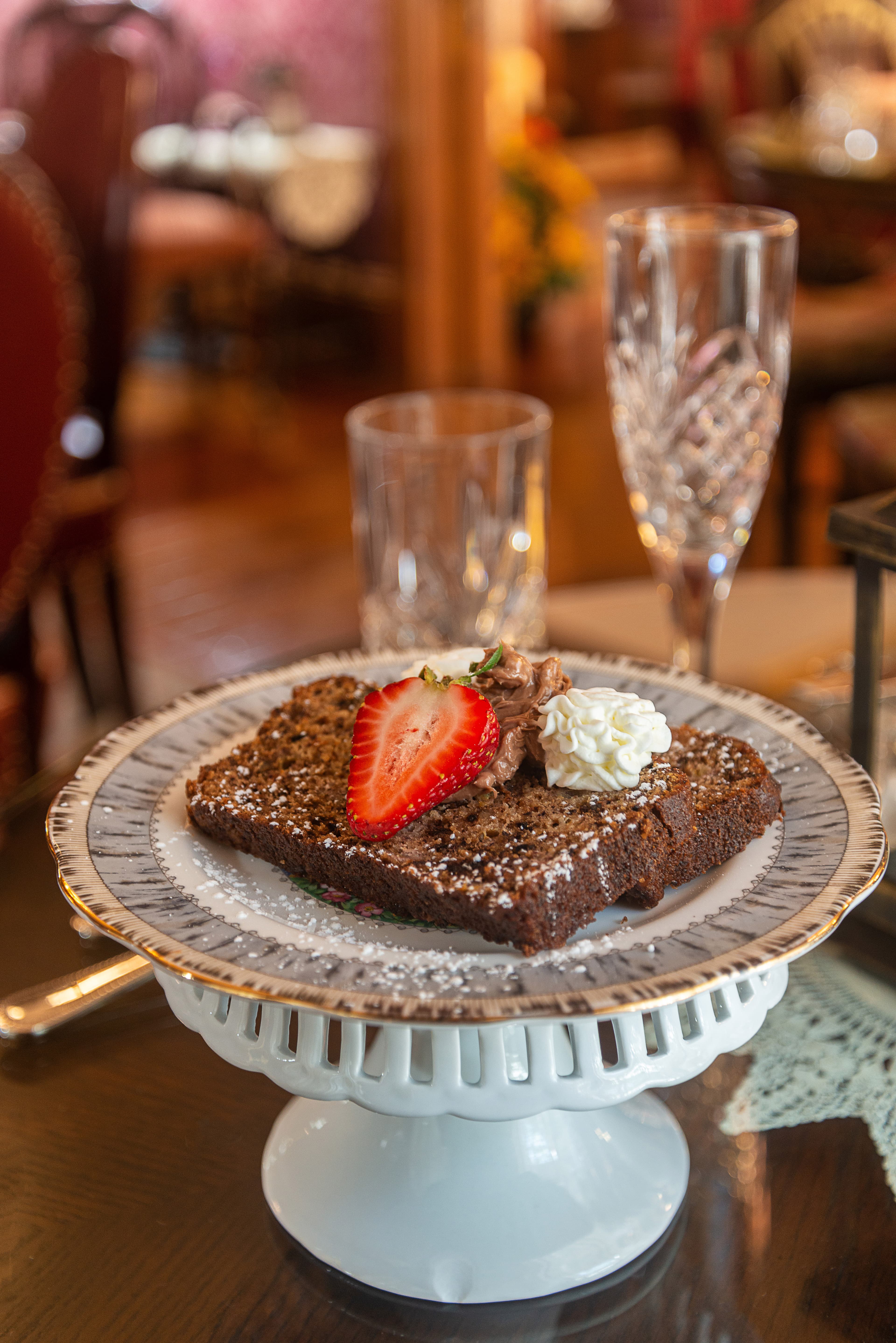 A slice of chocolate cake topped with a strawberry, whipped cream, and chocolate frosting, served on a decorative plate.