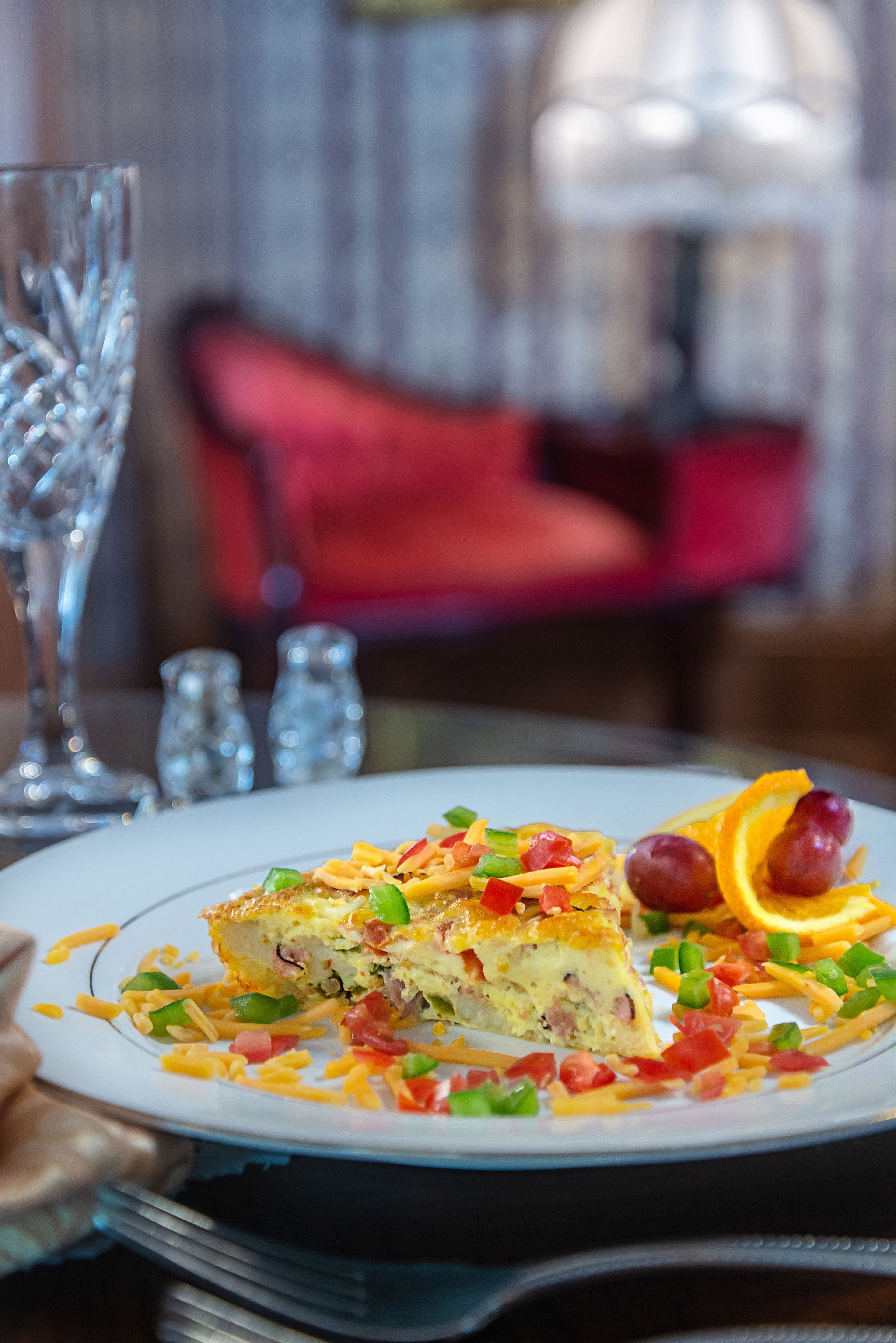 A plated omelette garnished with diced vegetables, cheese, and fruit sits on a table with elegant decor in the background.