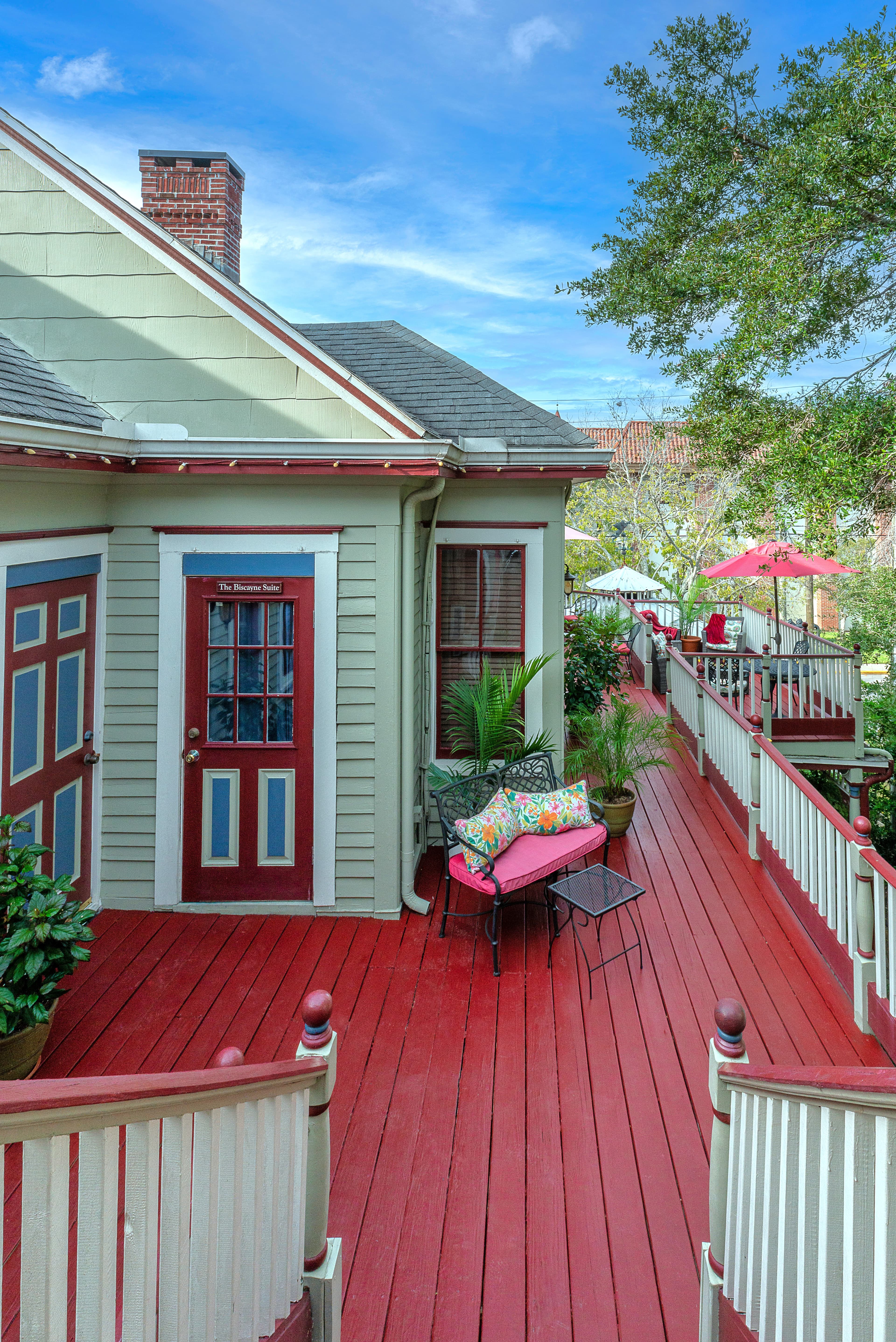Colorful patio area with green walls and red accents surrounded by greenery.