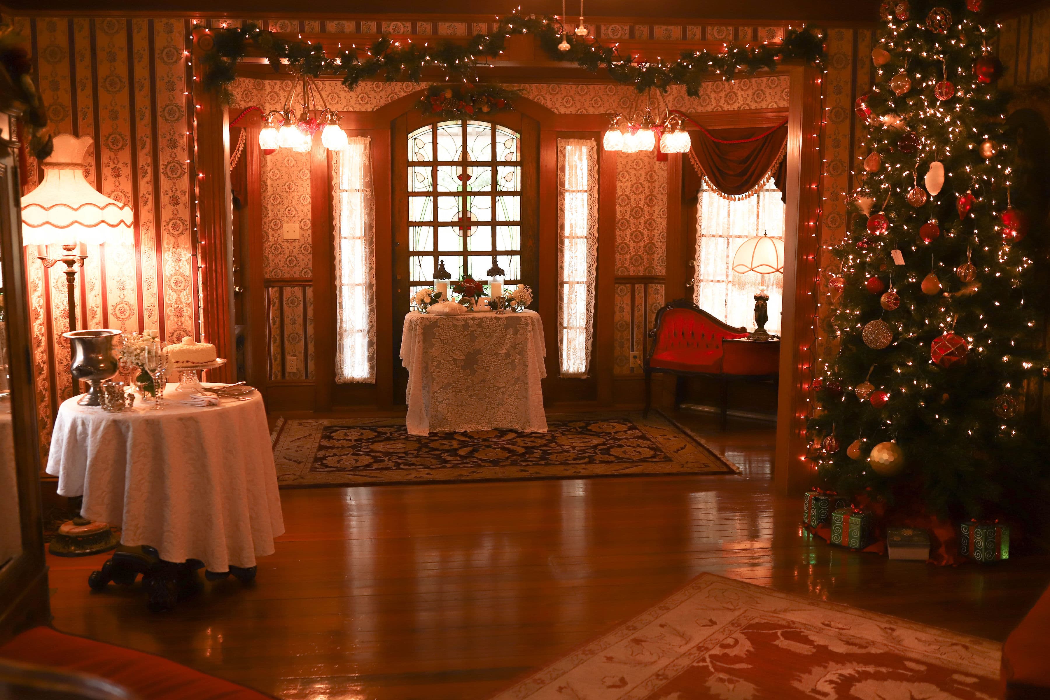 A cozy, festively decorated living room featuring a Christmas tree, elegant tables, and vintage furnishings.