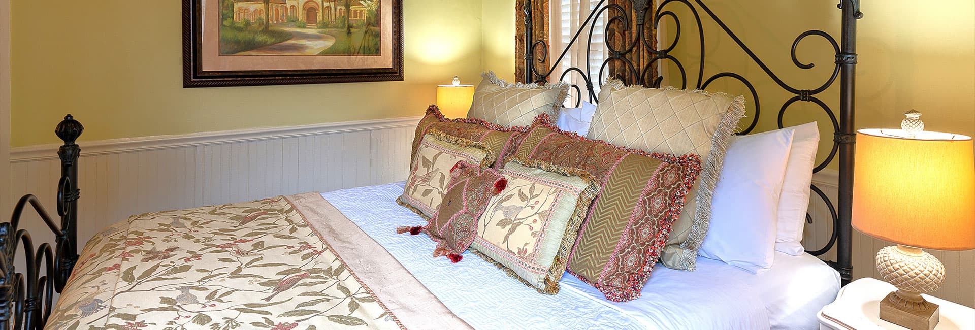 A cozy bedroom featuring a bed with decorative pillows, a warm lamp, and a framed painting on the wall.