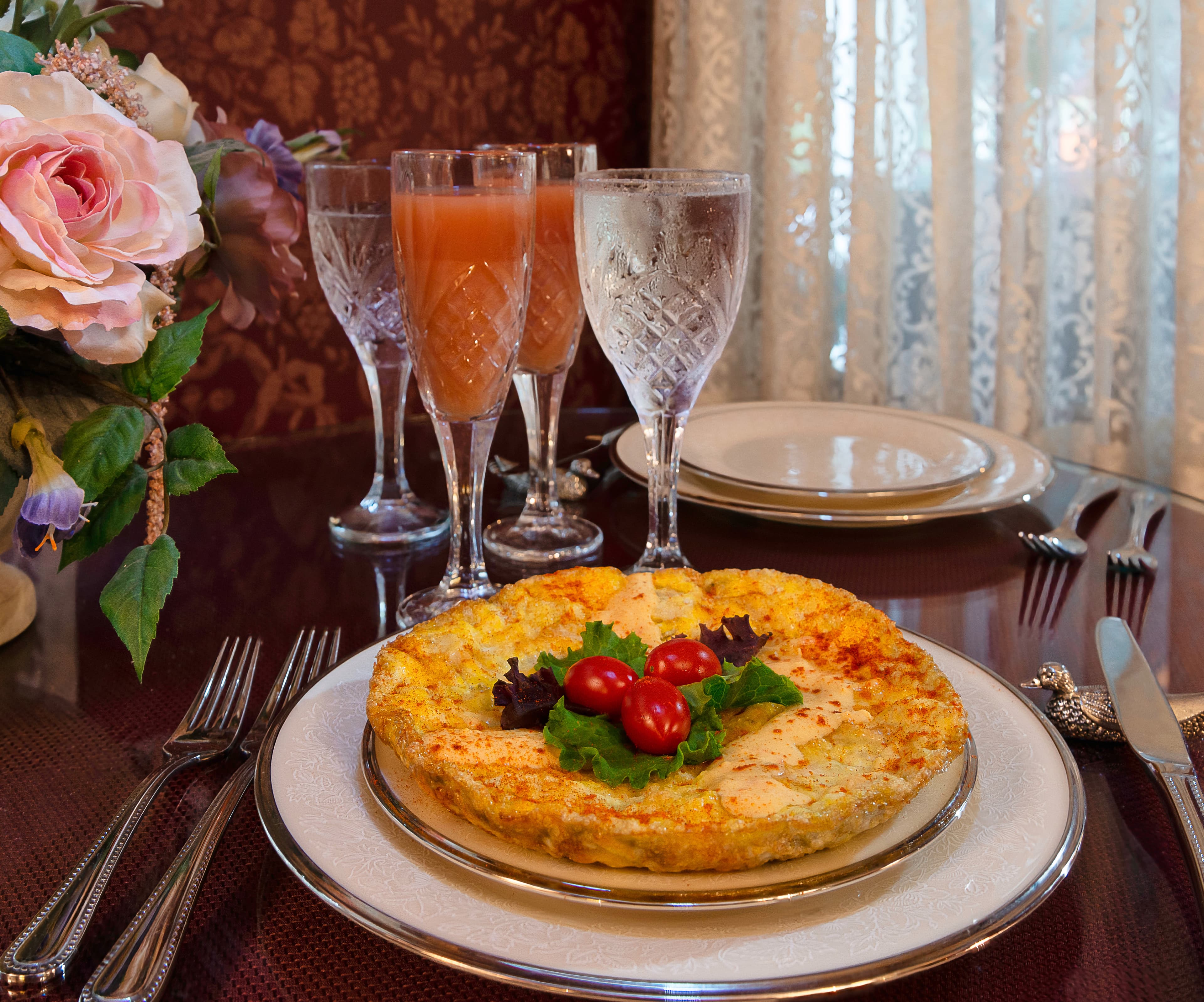 A beautifully arranged table featuring a colorful omelette garnished with cherry tomatoes and lettuce, accompanied by two glasses of fruit juice and iced water.