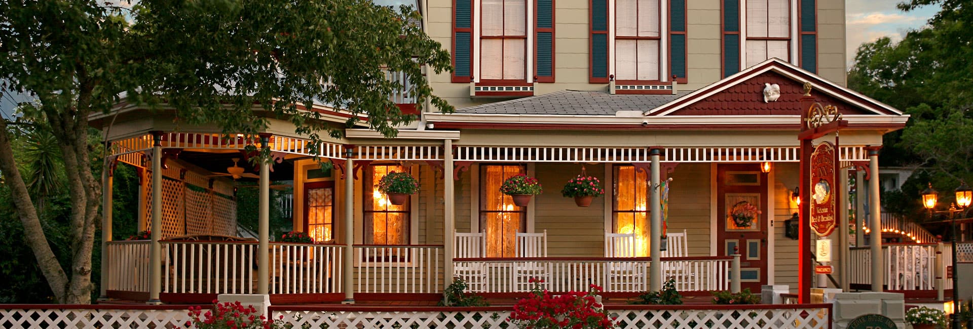 A charming inn featuring a wraparound porch adorned with hanging plants and rocking chairs.