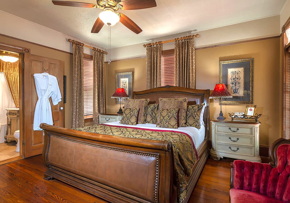 A cozy, elegantly decorated bedroom featuring a large bed, bedside lamps, and a plush armchair.