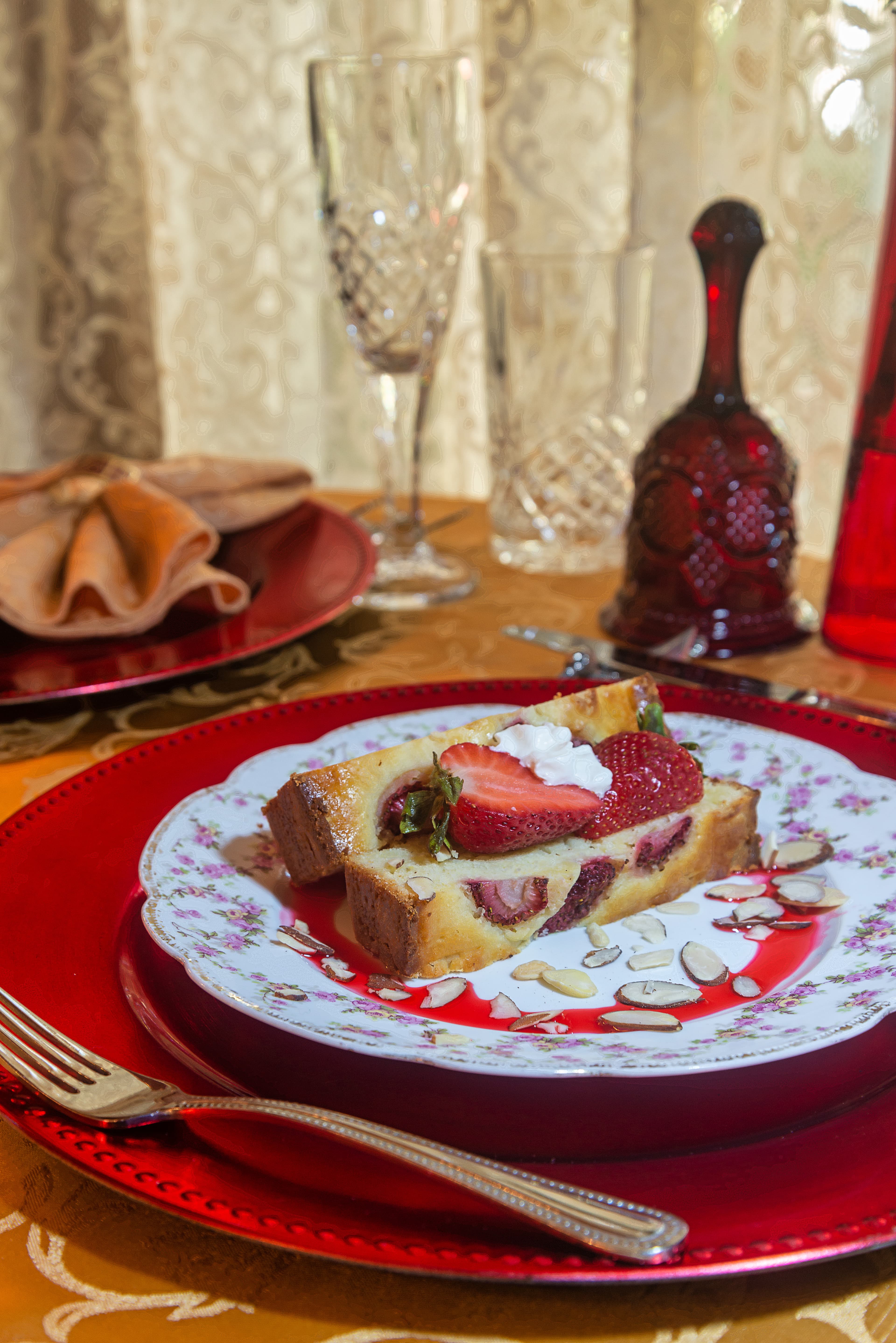 A decorative plate with slices of strawberry shortcake, garnished with whipped cream and sliced almonds, sits on a richly set table.