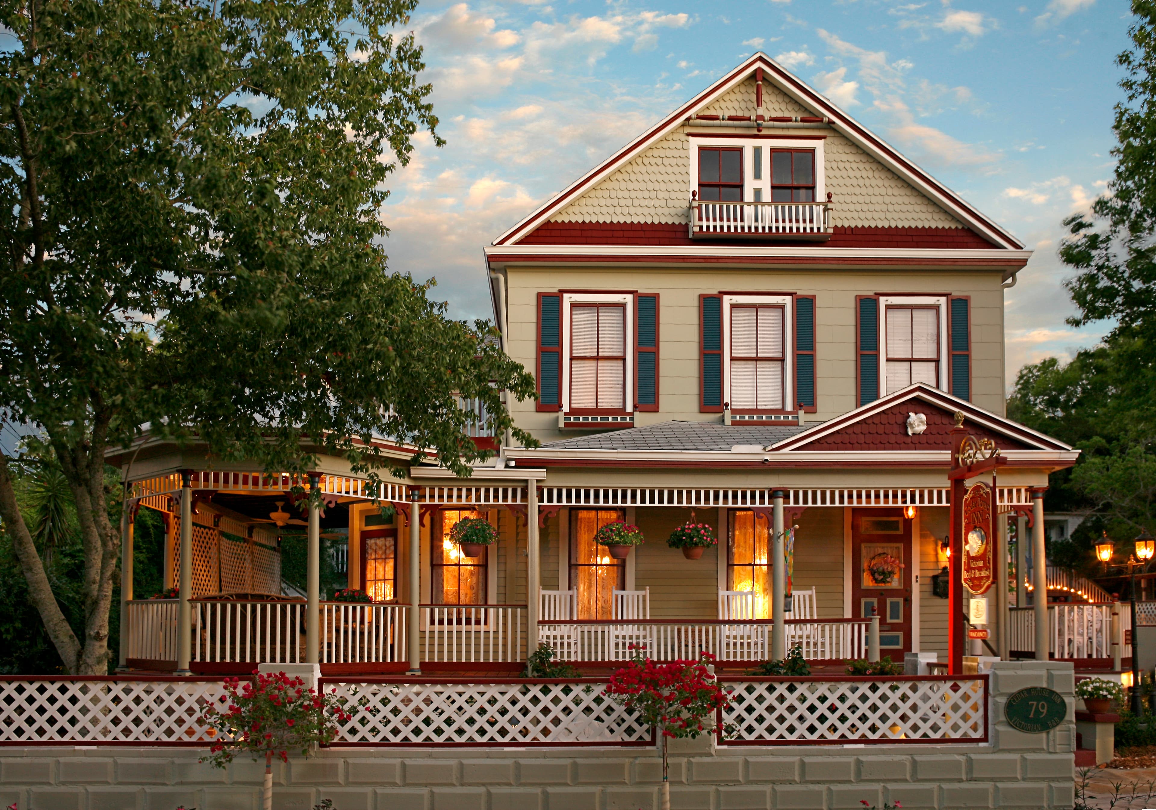 A charming, multi-story Victorian house with a wraparound porch and colorful flower planters.