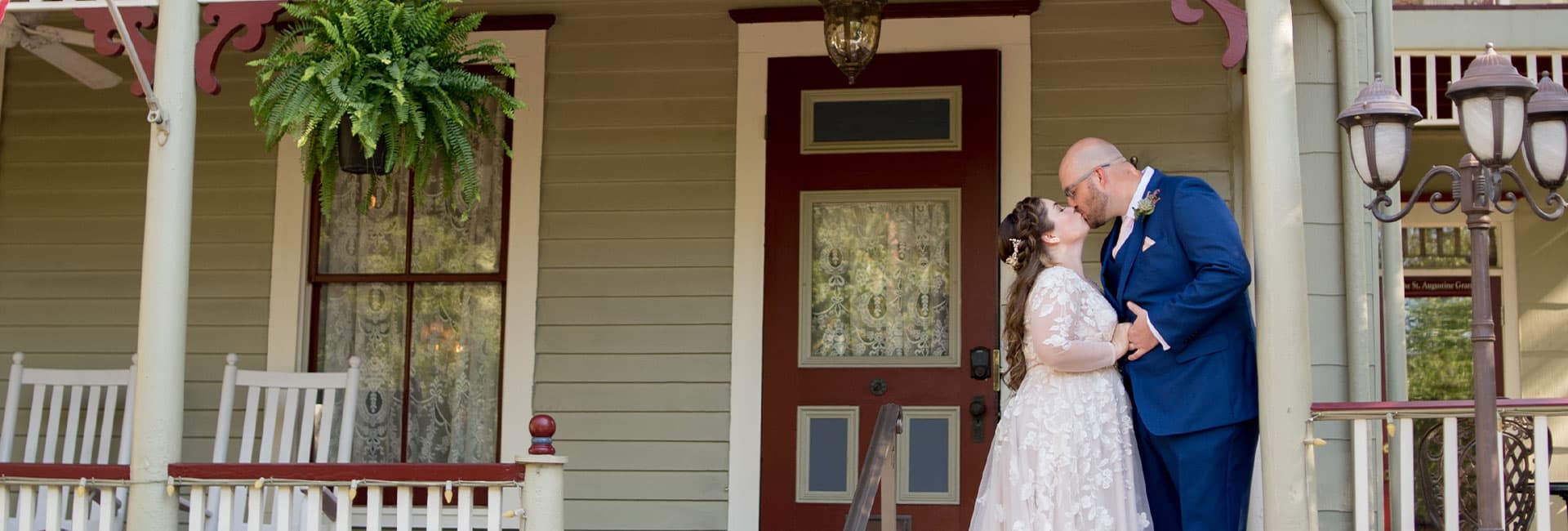 A couple shares a loving kiss on the porch of a vintage house.