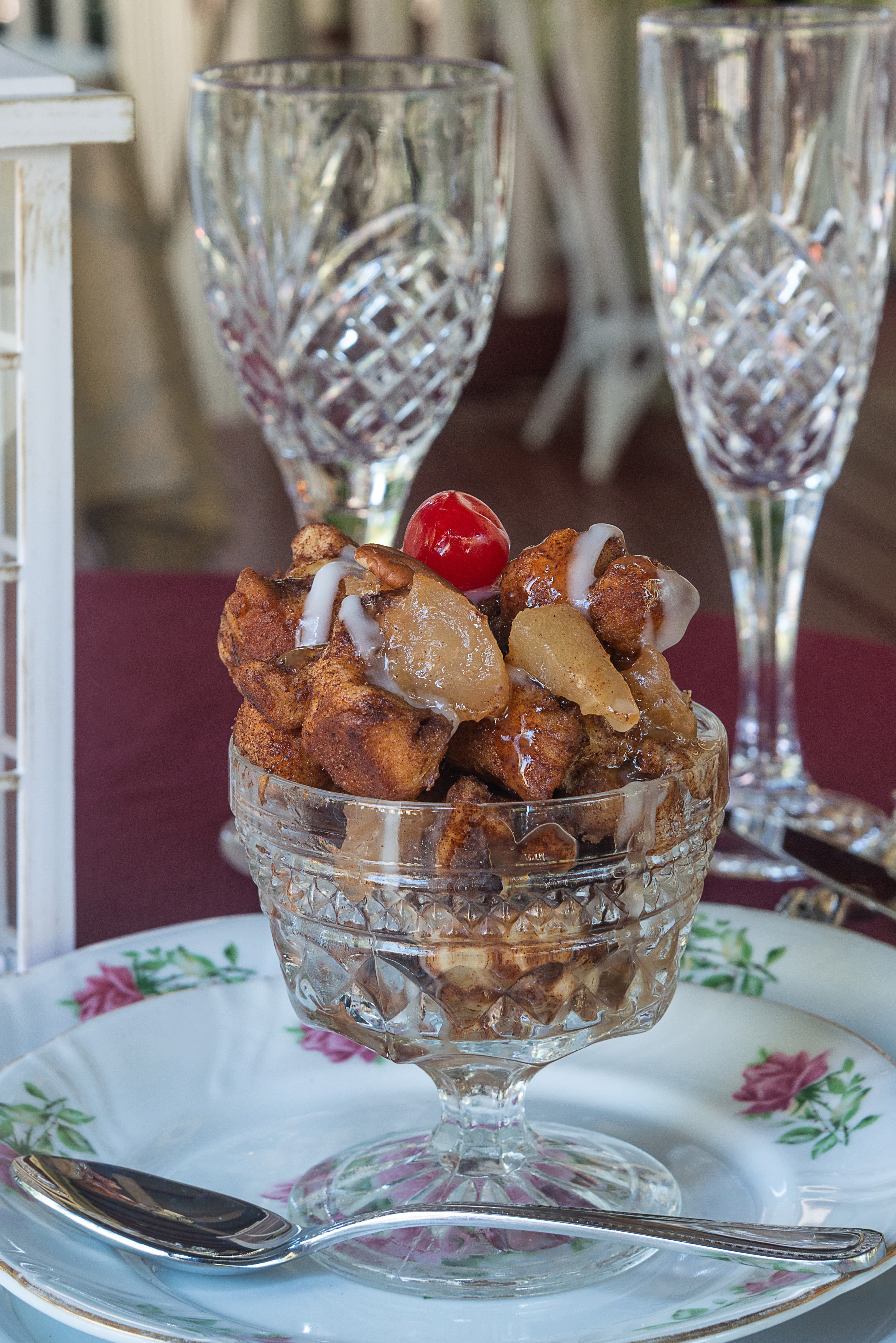A glass dish filled with bread pudding topped with apples, a cherry, and drizzled with icing.