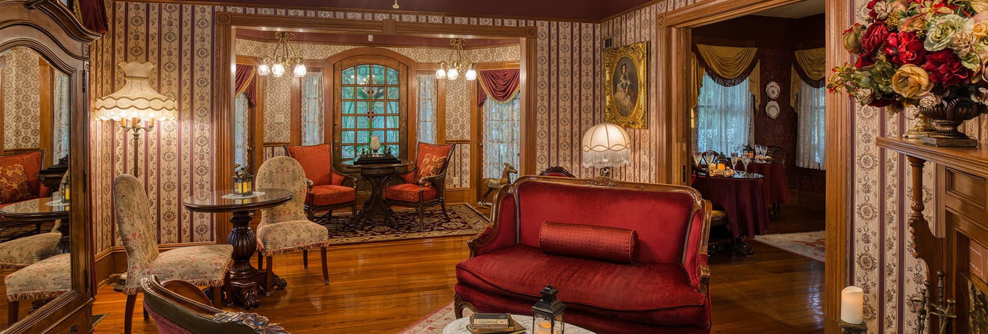 A cozy, vintage-style living room featuring ornate wallpaper, plush seating, and warm lighting.