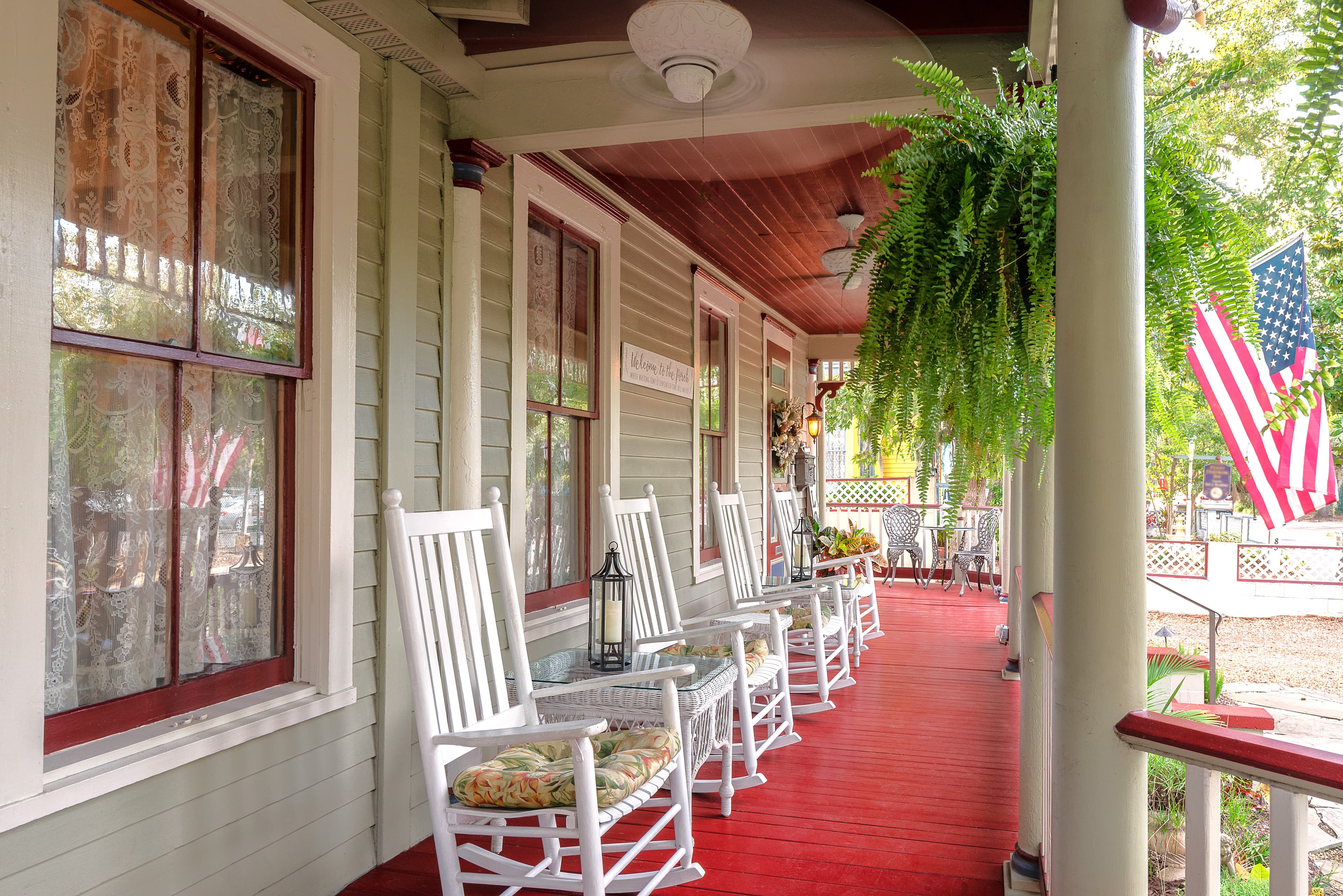 A charming porch with rocking chairs, potted ferns, and an American flag.