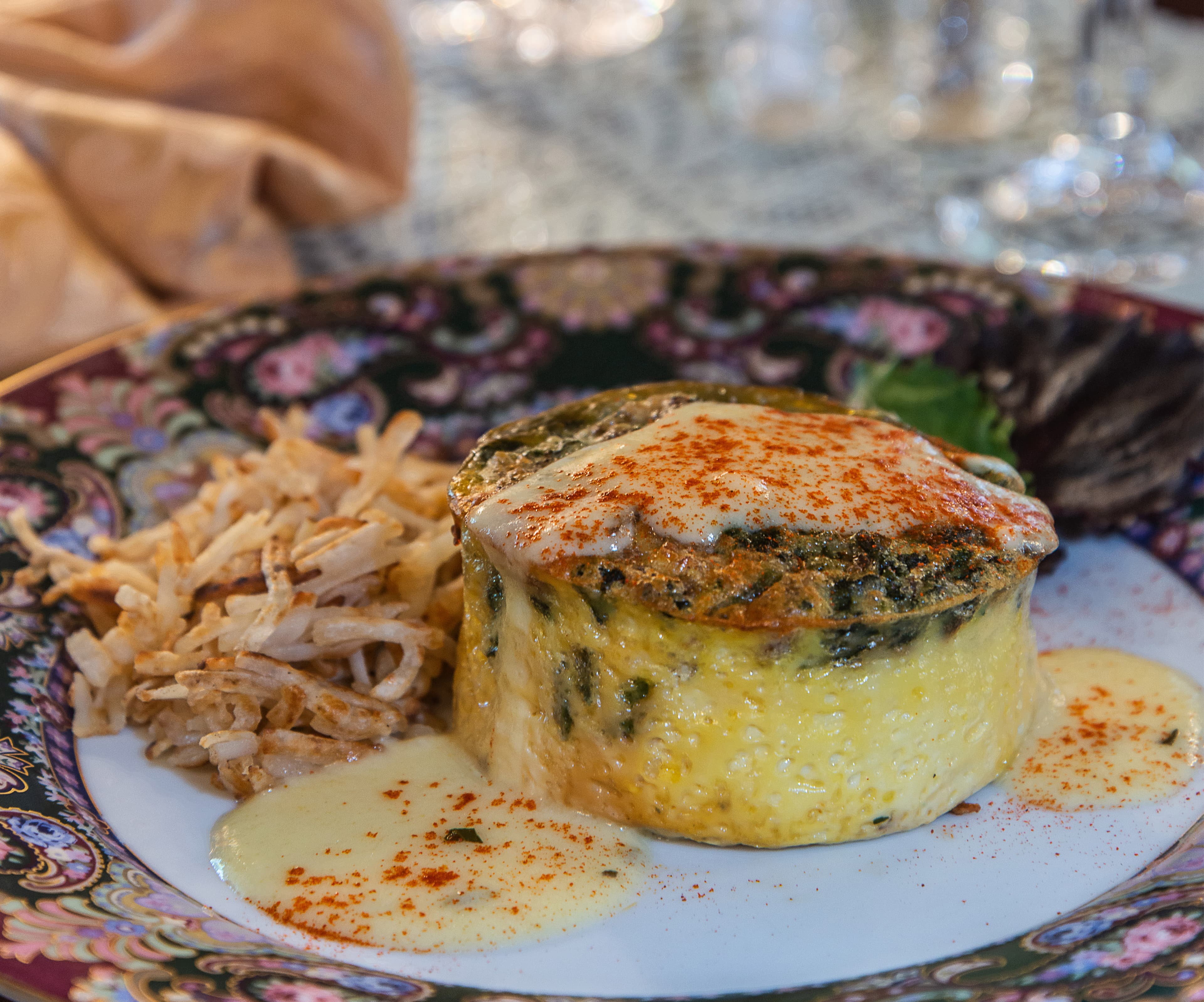 A creamy spinach souffle garnished with paprika, served alongside crispy potato straws on a decorative plate.