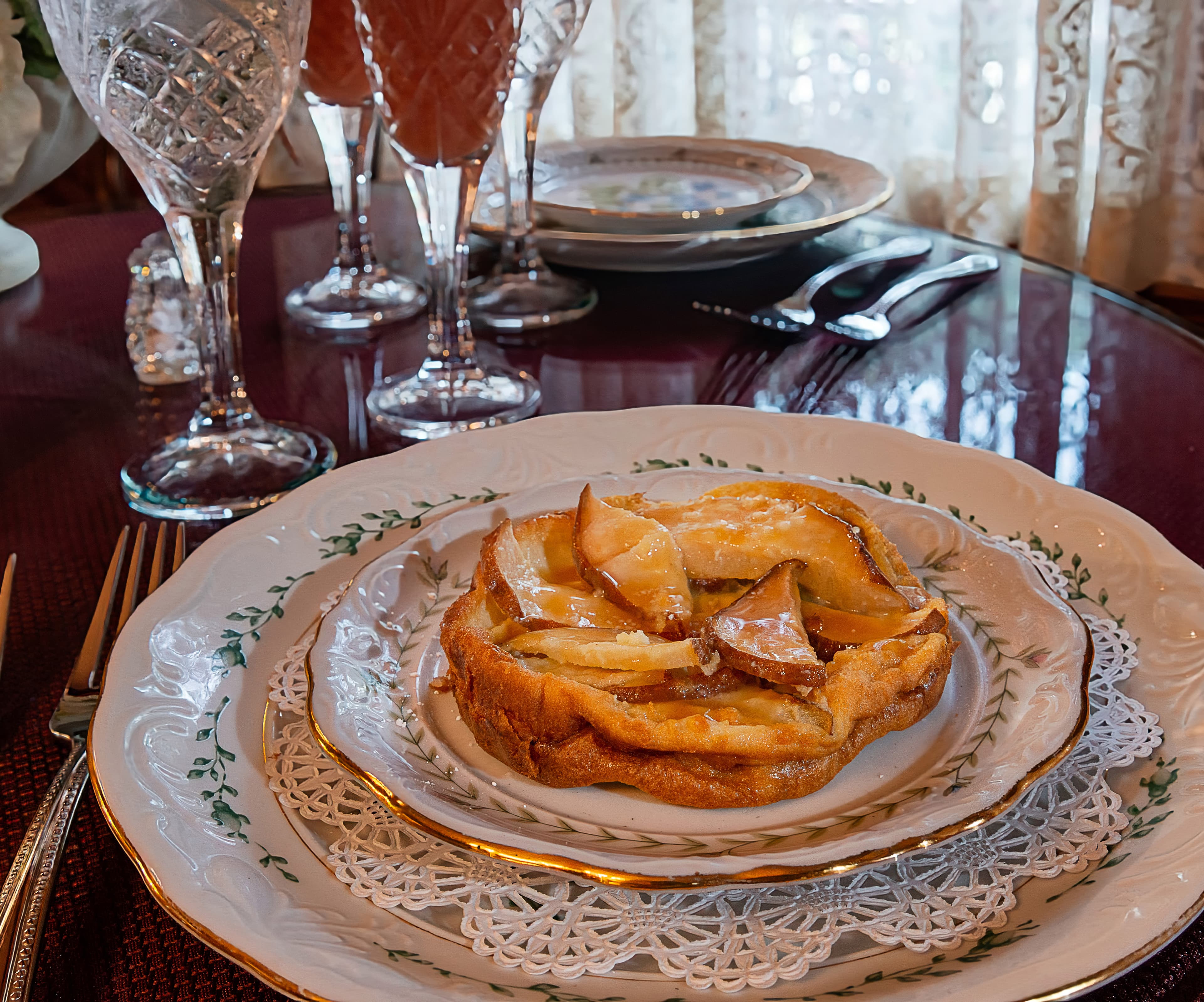 A slice of apple tart is artfully presented on an elegant plate, surrounded by sparkling drinks and fine diningware.