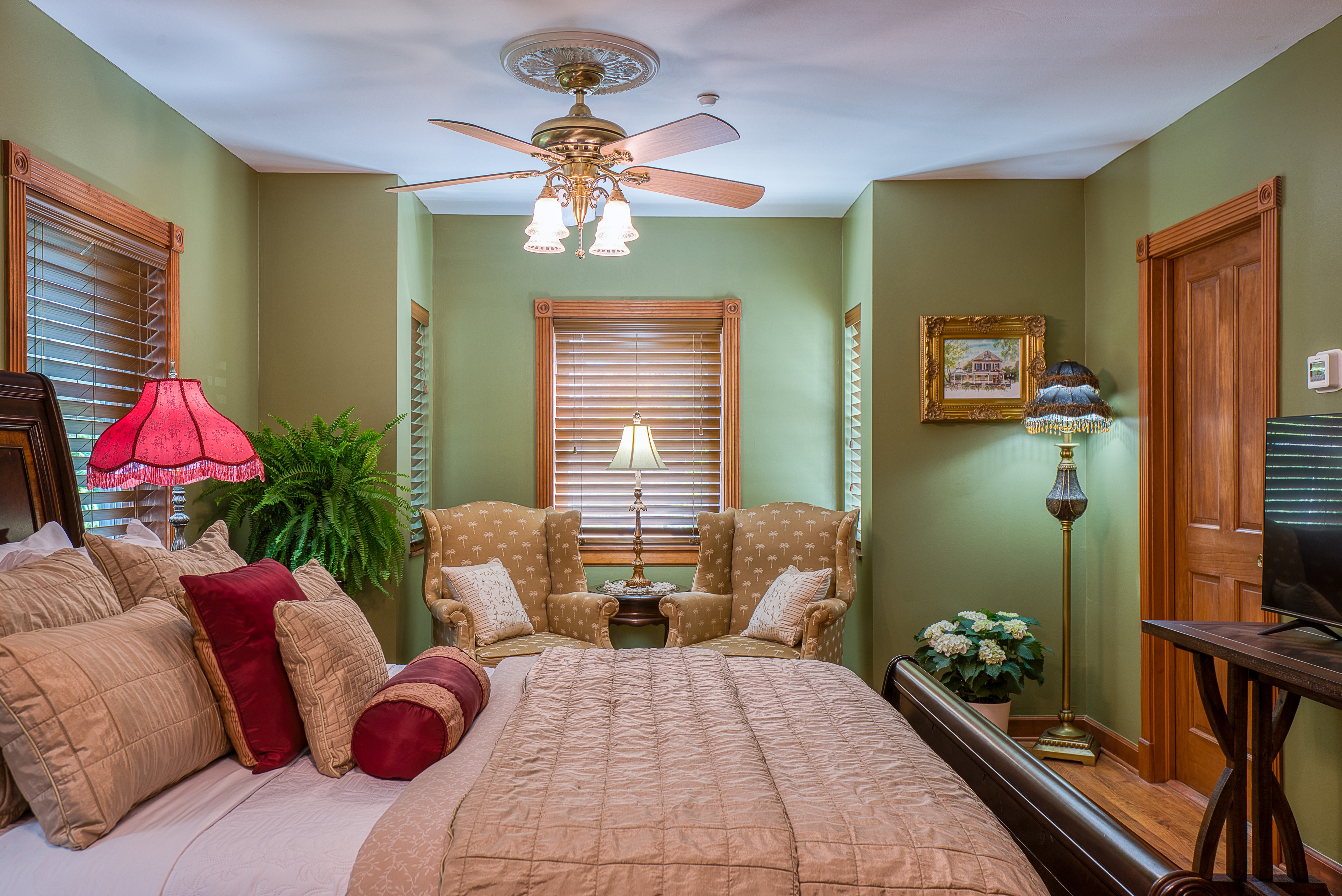 A traditionally styled bedroom with a dark wood bed frame, a sitting area with two armchairs, and a window with a wooden frame.