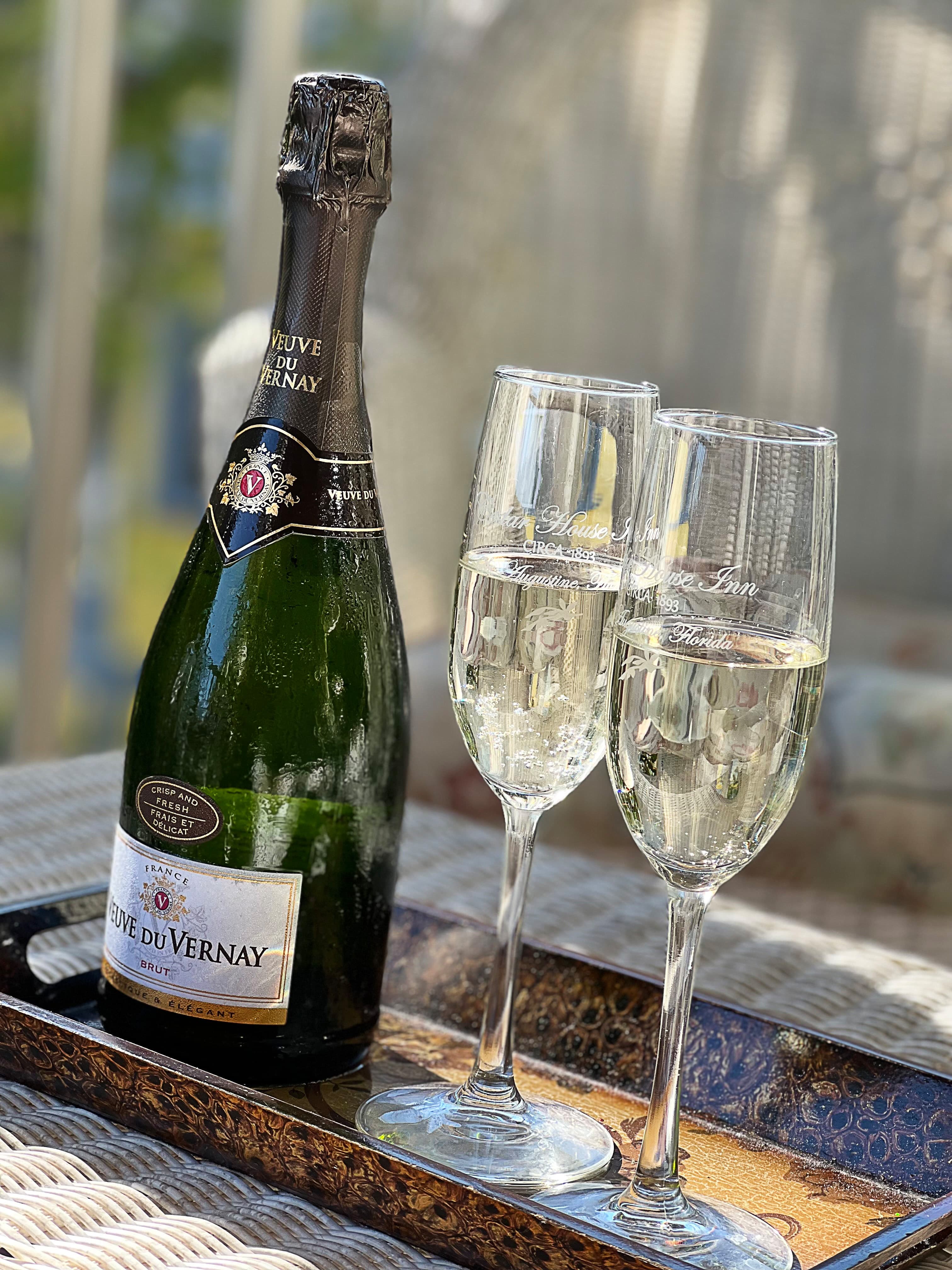 Close-up view of a bottle of champagne and two champagne glasses filled with champagne, placed on a tray with a decorative pattern.