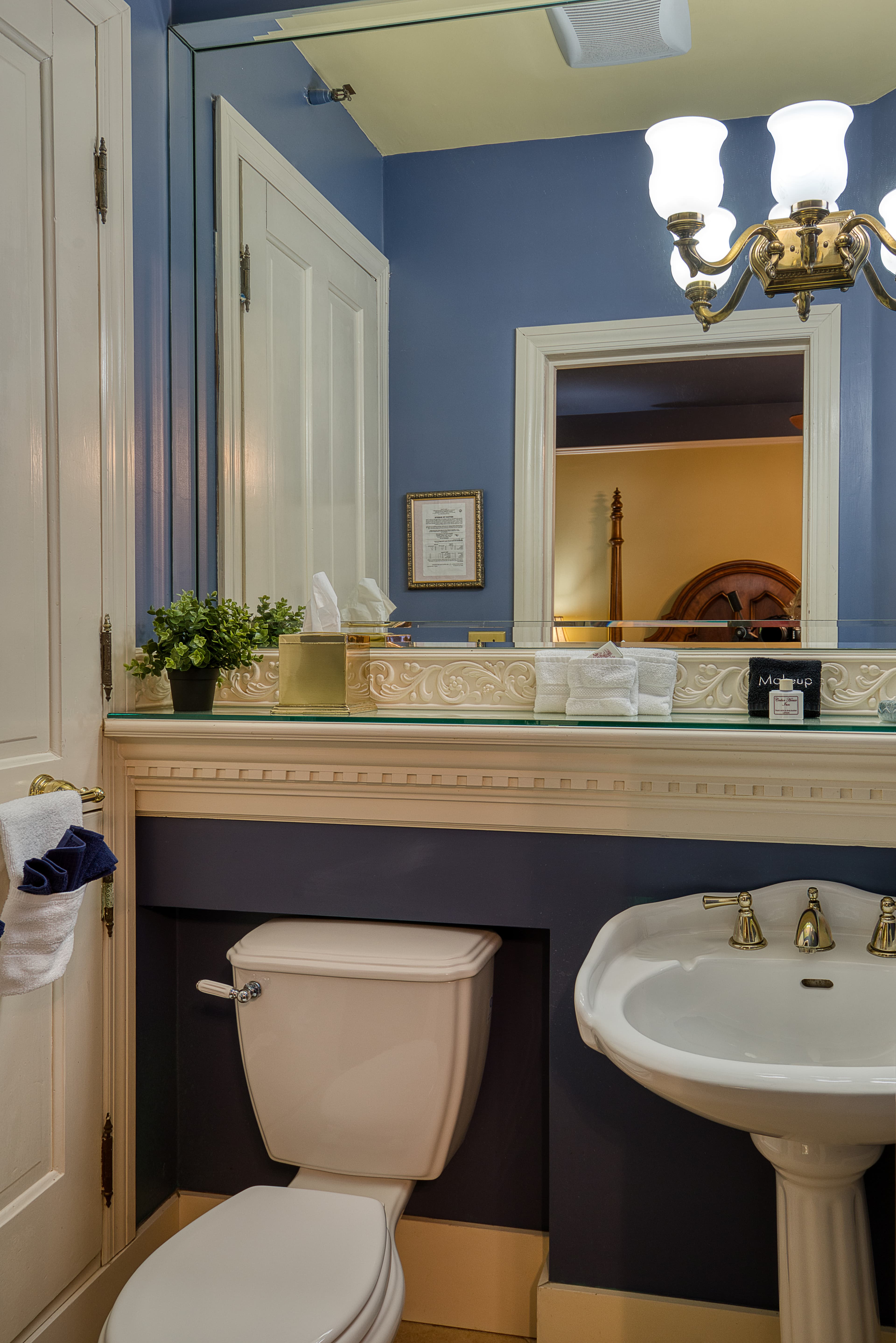 Bathroom featuring a sink with a chrome faucet, a toilet, and a large mirror above the sink with a light fixture. The walls are painted blue, and the floor is tiled.