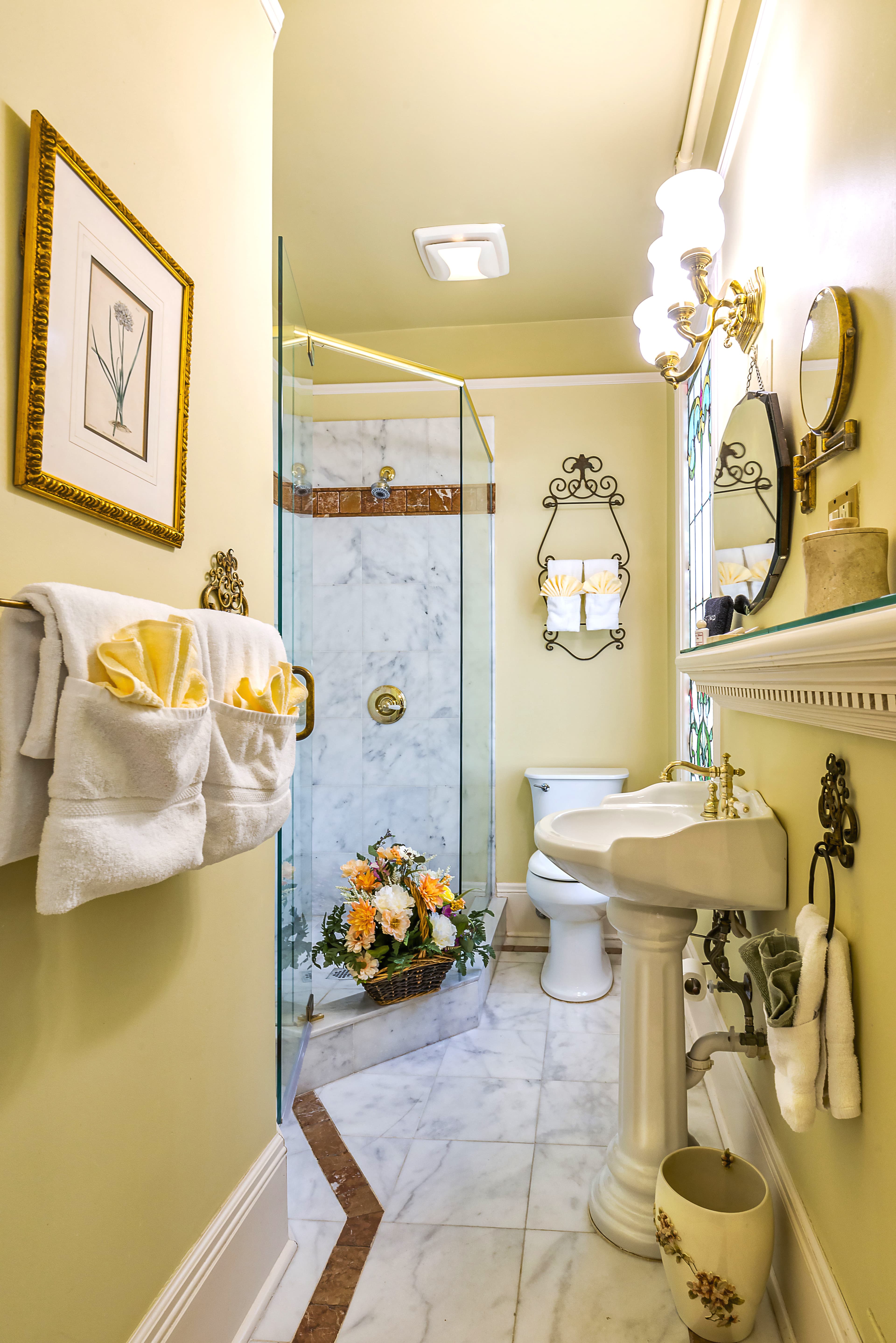 Interior view of a bathroom featuring a shower with a glass door, a toilet, and a sink with a chrome faucet. The walls are painted yellow, and the floor is tiled.