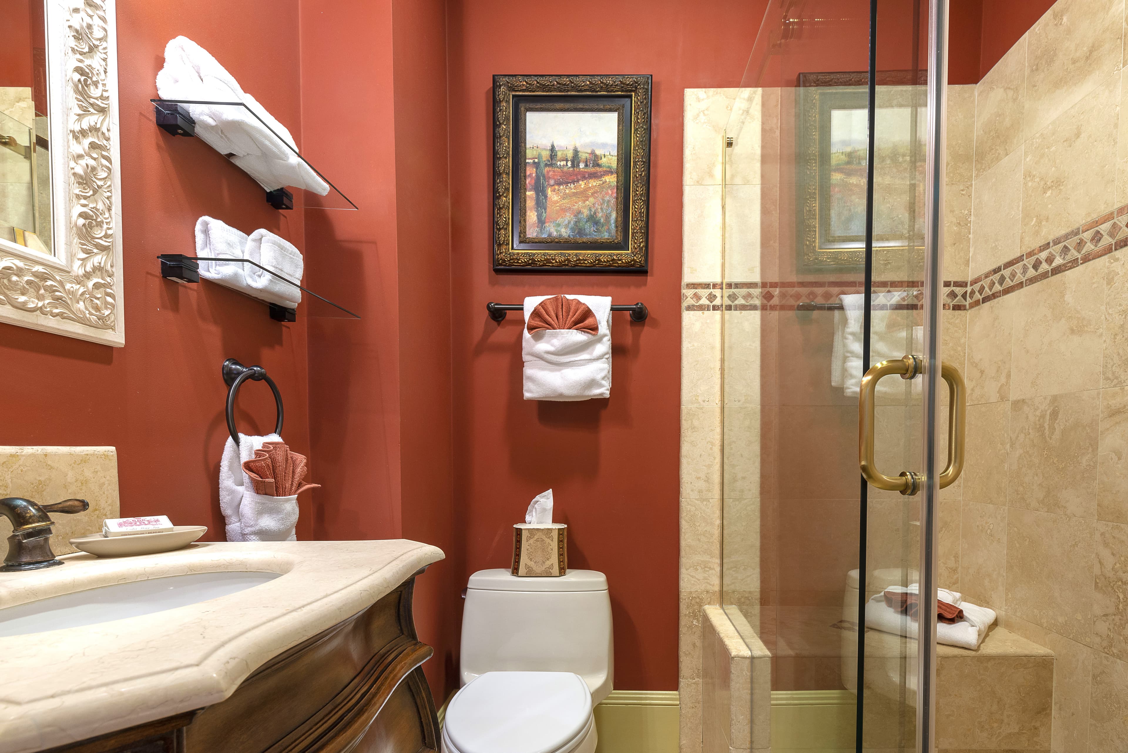 Elegant bathroom featuring a shower with a glass door, a toilet, and a sink with a chrome faucet. The walls are painted red, and the floor is tiled.