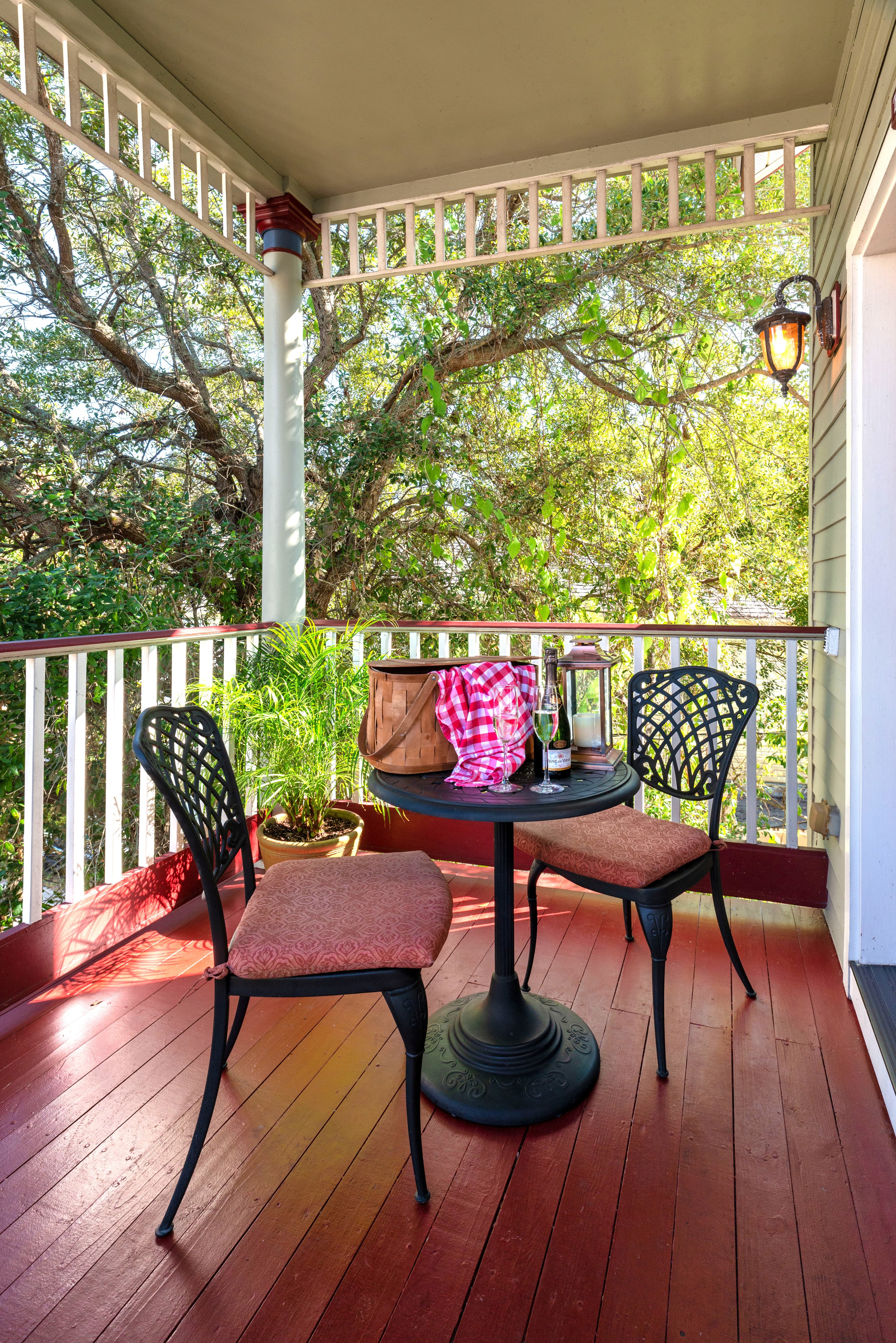 Exterior view of a balcony featuring a table with chairs, surrounded by lush greenery and colorful flowers.