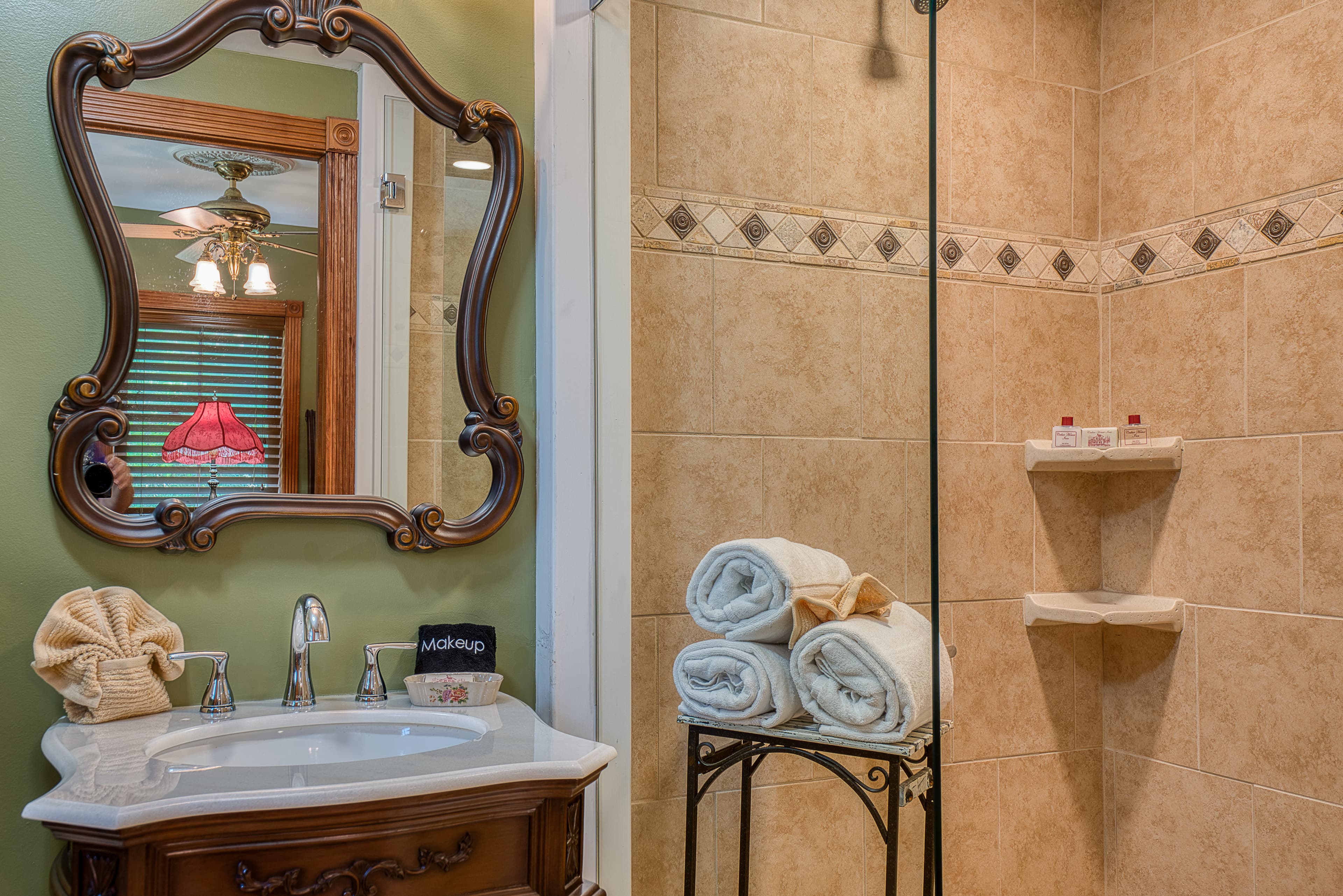 A bathroom with a dark wood vanity with a white countertop and sink, a decorative mirror, and a shower with a glass enclosure.