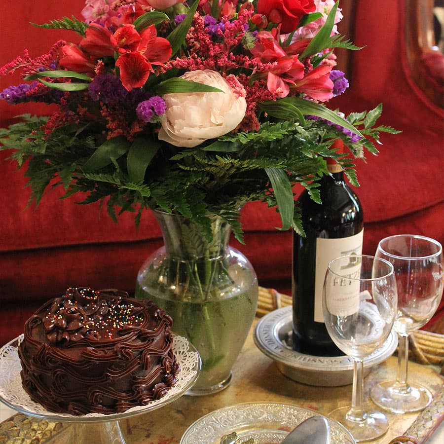 A beautiful arrangement of colorful flowers, a chocolate cake, a bottle of wine, and elegant glassware on a table.