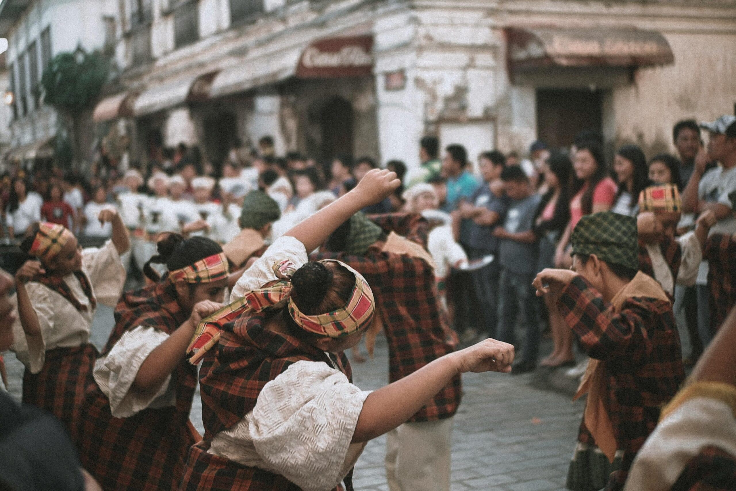 A group of performers in traditional clothing dances in a street while a crowd watches.