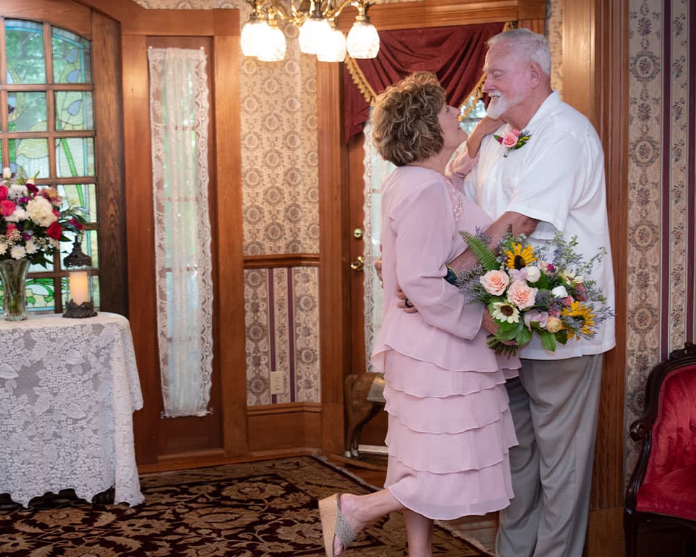 A couple shares a joyful moment indoors, surrounded by floral arrangements and warm wooden furnishings.