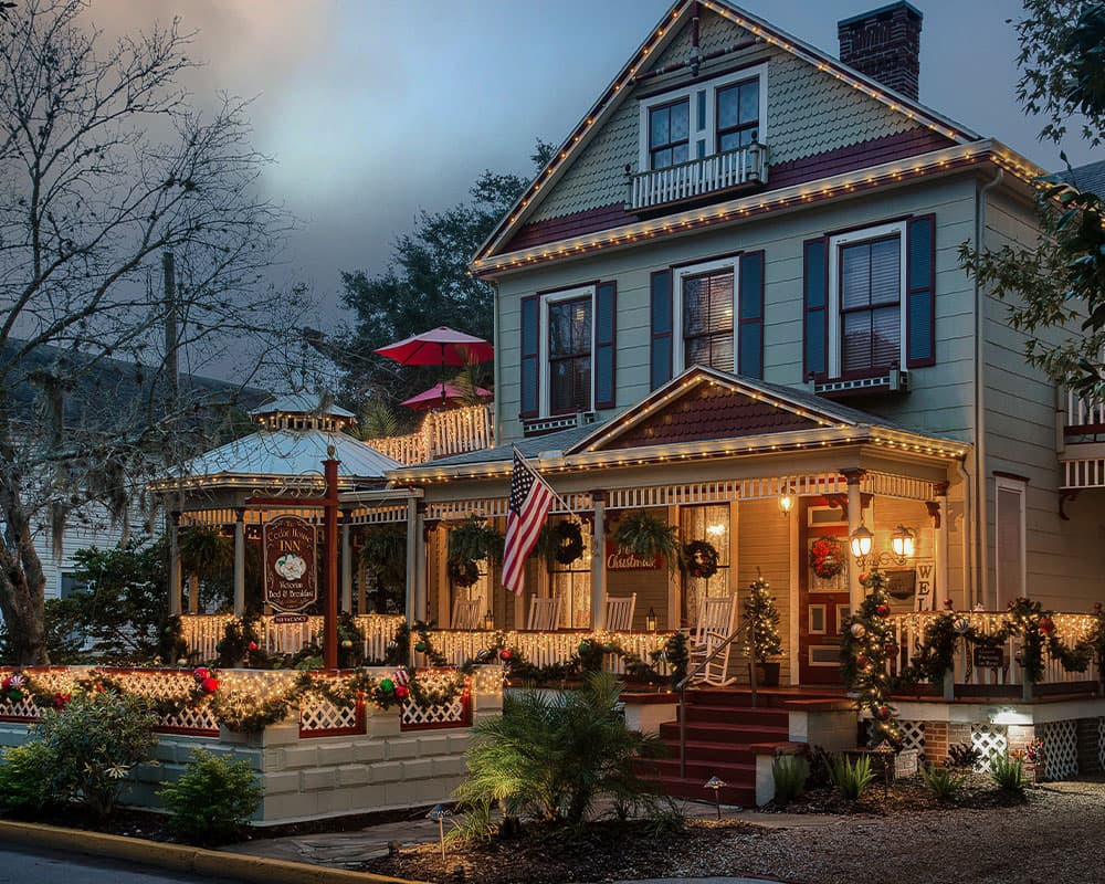 A beautifully decorated Victorian inn adorned with holiday lights and festive greenery.
