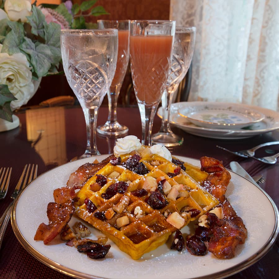 A plate of waffles topped with fruit, nuts, and whipped cream, accompanied by glasses of sparkling drinks.